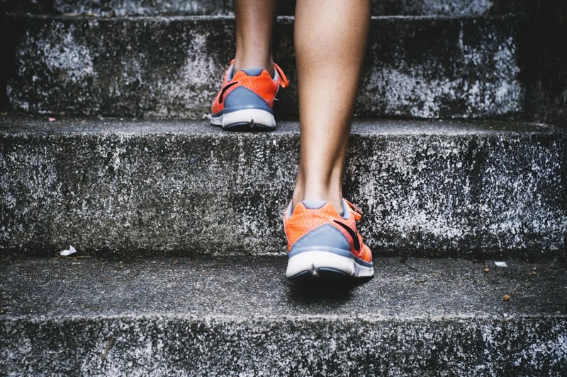Close-up from behind of orange athletic shoes stepping up weathered concrete outdoor stairs
